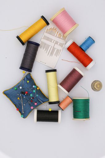 A vertical shot of colorful threads and needles on the table under the lights - fashion concept