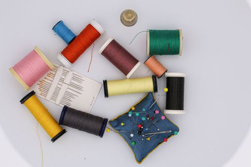 A high angle shot of colorful threads and needles on the table under the lights - fashion concept