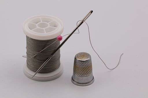 A closeup shot of a needle on a grey thread on the table with a thimble on it - sewing concept
