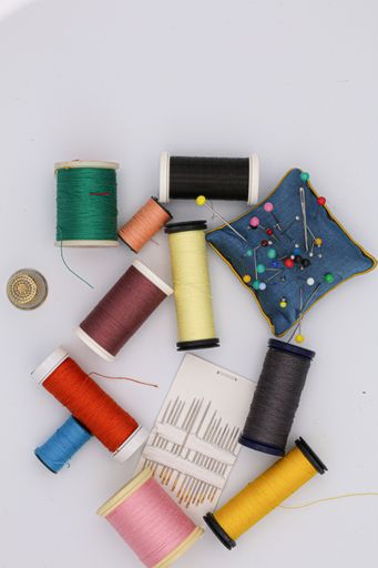 A vertical shot of colorful threads and needles on the table under the lights - fashion concept