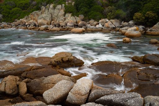 A river with long exposure surrounded by rocks and greenery under the sunlight at daytime