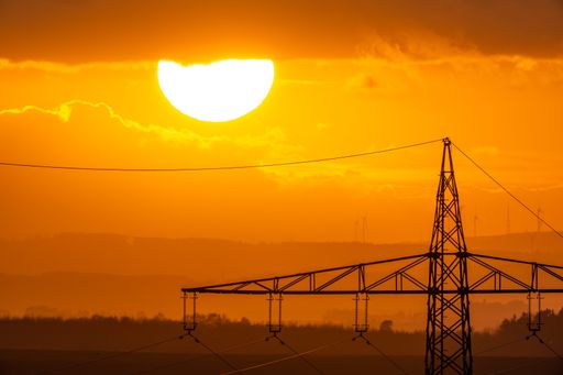 A view of a transmission tower against the orange sun setting down