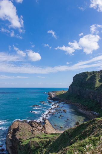 A high angle shot of the ocean waves crashing against the rocky coastline covered with greenery in Chaojing Park, Taiwan