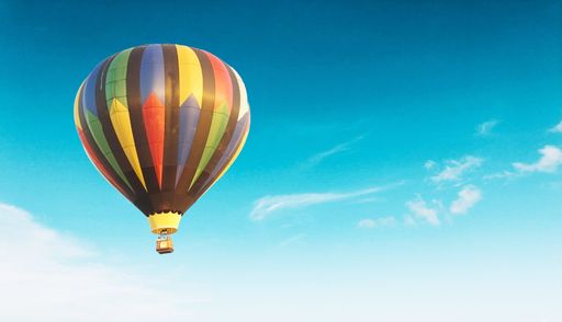 A colorful air baloon flying high in the blue sky with clouds floating around it
