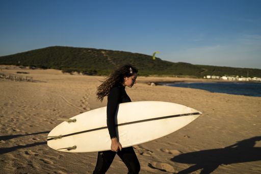 A shallow focus shot of an attractive female carrying a surfboard while walking at the seashore in Spain