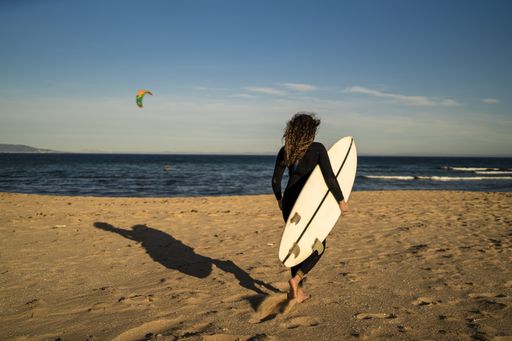 A shallow focus shot of a female carrying a surfboard while walking at the seashore in Spain