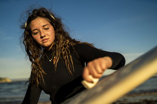 A selective focus shot of an attractive female waxing her surfboard at the beach in Spain