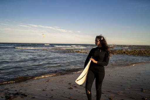 A shallow focus shot of an attractive female carrying a surfboard while walking at the seashore in Spain