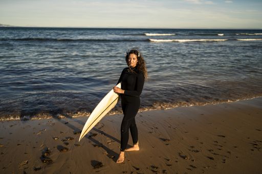A shallow focus shot of an attractive female carrying a surfboard while standing at the seashore in Spain