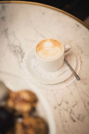 A vertical shot of a cup of cappuccino on the marble table with desserts