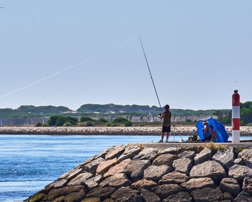 A view of a man standing on a rocky coast and fishing on a sunny day at Ria de Aveiro, Portugal