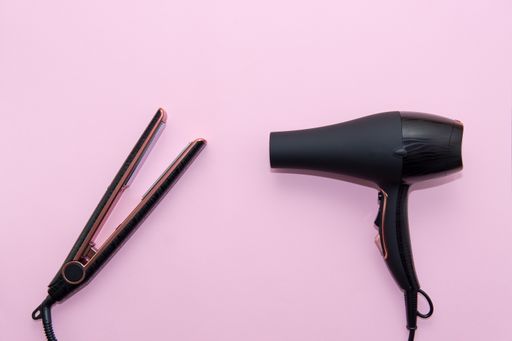 Top view of black hair straightening iron and a hairdryer on pink background. Hair care concept, copy space