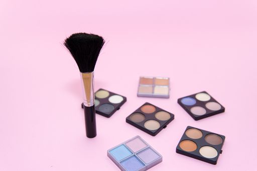 Make-up set with various colors and a brush on pink background. Beauty concept, copy space