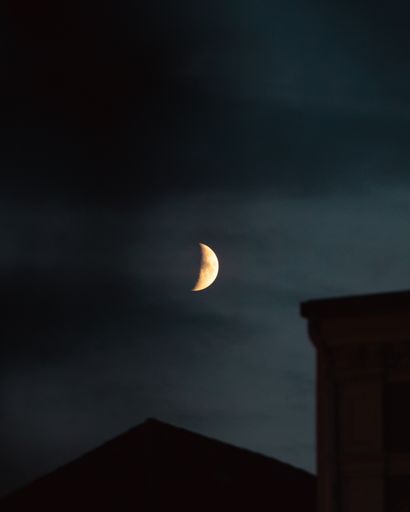 A vertical shot of the half moon in the cloudy skies