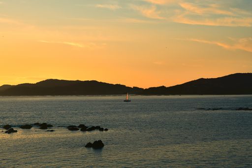 A breathtaking shot of the sailboat in the sea and the hills gleaming under the golden sunset