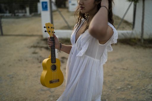 A closeup shot of a female in a white dress holding a yellow ukulele