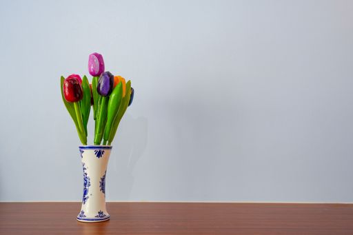 A photo of tulips in a vase on a wooden table against a white background