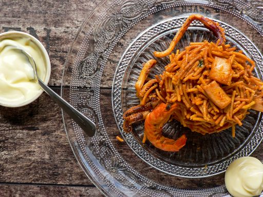 A top view of noodle paella a typical Catalan dish made with noodles and seafood with garlic sauce and oil on a glass plate