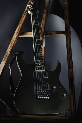 A vertical shot of a black, electric guitar leaning on wooden sticks