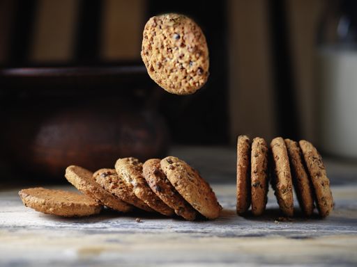 A line of chocolate chip cookies with one of them flying, isolated on a blurred background
