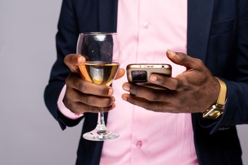 An African American male using his phone while holding a glass of wine