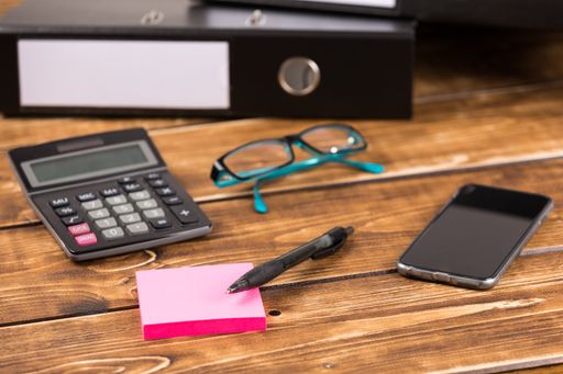 A closeup shot of a desk with folder, smartphone, glasses, and calculator