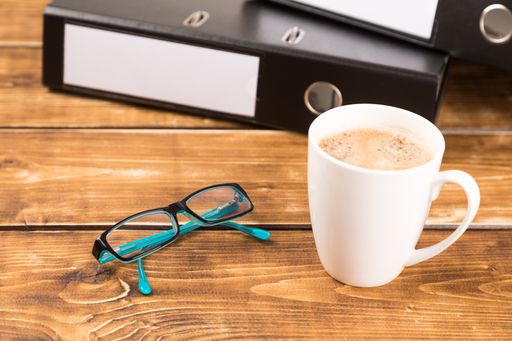 A closeup shot of a business desk with coffee cup, glasses, and folder