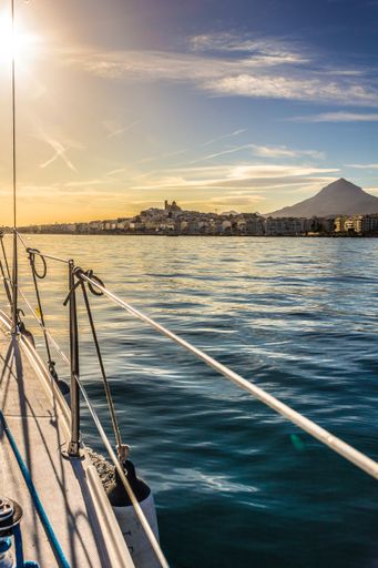 A vertical shot of mountain and buildings seen from a ship during sunset