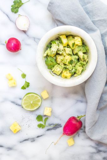 An overhead vertical shot of pineapple guacamole in a white bowl near lemons