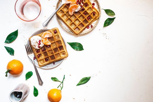 An overhead shot of waffles with orange slices on a white plate near forks