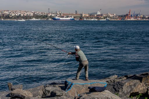 A man standing on the stone on the lakeshore and fishing