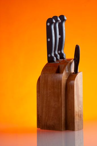 A vertical closeup of a set of kitchen knives isolated on an orange background