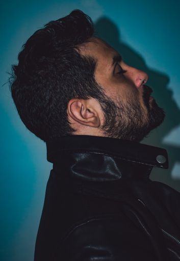 A vertical shot of a male standing in front of a blue wall with his shadow reflecting