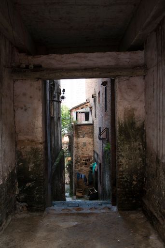 A vertical shot of an empty street between old rustic abandoned houses covered with moss
