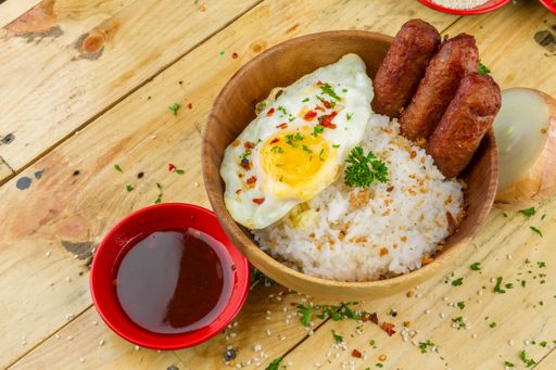 Some rice, omelet and sausages with seasonings served in a bowl and souse nearby