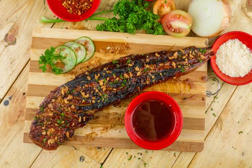 A big piece of roasted meat with garnish, souse and cucumbers served on a wooden tray