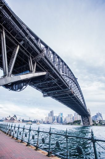 A low angle vertical shot of a bridge over the water with city buildings in the distance under a cloudy sky