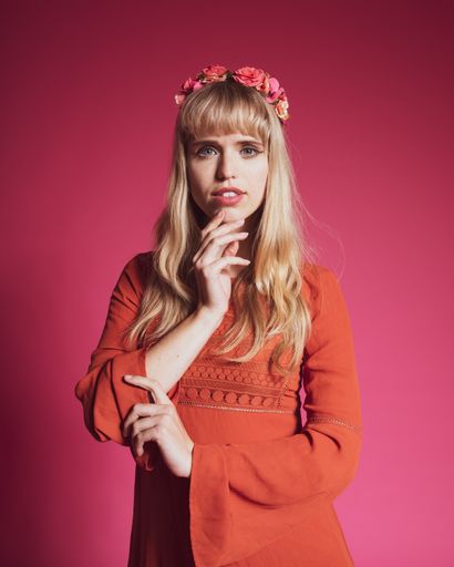 A portrait of an attractive woman with a flower crown posing on a pink background