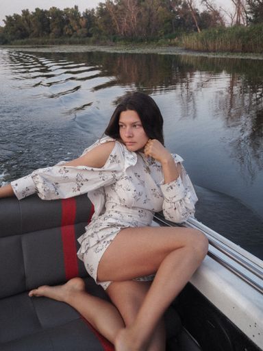 A vertical shot of a woman in a short white dress sailing on a boat through a lake