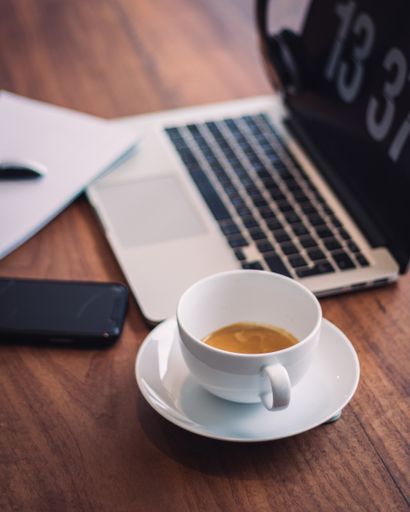 A vertical shot of a cup of coffee beside a laptop