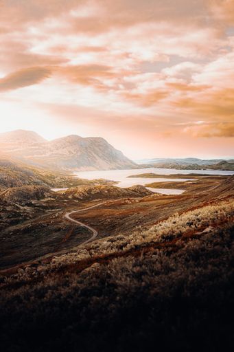 A vertical shot of a lake surrounded by mountains covered by greenery under the sunset cloudy sky