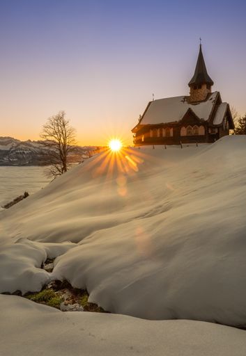 A vertical shot of the beautiful church in the snow at the sunset in Swiss Mountains