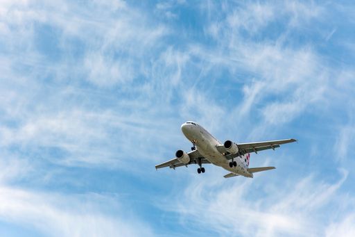 A passenger jet airplane in mid-flight against blue sky with clouds, getting ready for landing.