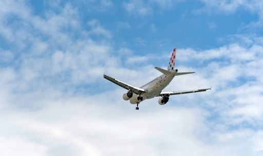 A passenger jet airplane in mid-flight against blue sky with clouds, getting ready for landing.