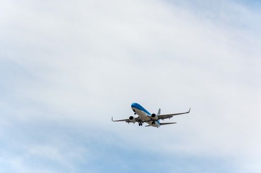 A passenger jet airplane in mid-flight against blue sky with clouds, getting ready for landing.
