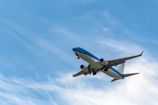 A passenger jet airplane in mid-flight against blue sky with clouds, getting ready for landing.