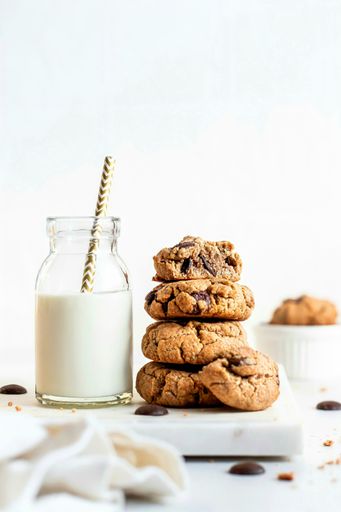 A closeup of a milk bottle with straw and cookies on a white table