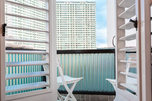 A view of a building on the background with an sky hint from a balcony with 2 small chairs.