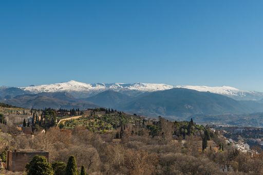 View of the walls and gardens of the Alhambra under the snow-capped mountains of the Sierra Nevada in Granada, Spain.