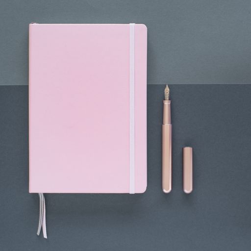 A flat lay of a pink notepad and an open pen